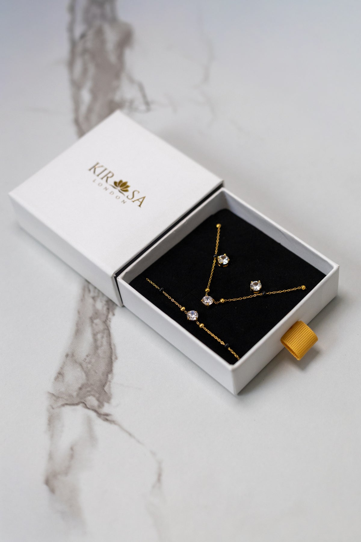 Kirasa London Avira 3-piece gold jewelry gift set with solitaire crystal necklace, bracelet, and stud earrings in display packaging.