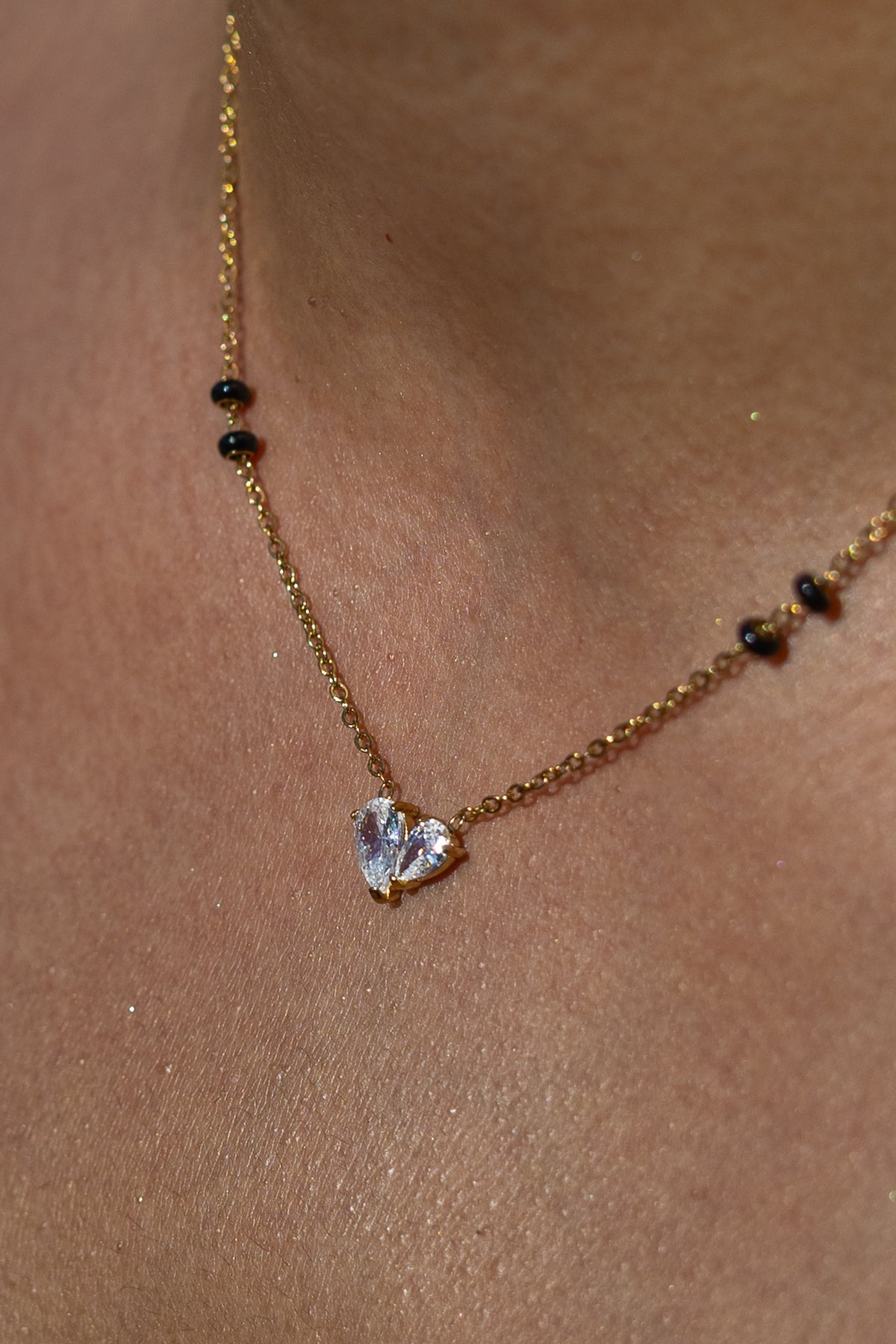 Close-up of a model wearing a Kirosa London gold mangalsutra necklace featuring a heart-shaped dual pear-cut crystal pendant flanked by signature black beads.