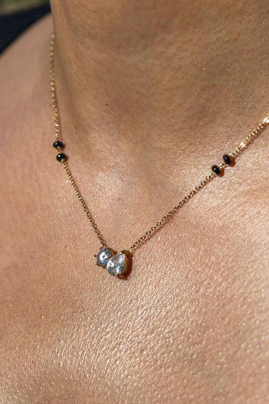 Close-up of a model wearing the Kirasa London gold Ananta Mangalsutra Necklace featuring a two-stone round and pear-cut crystal pendant flanked by signature black beads. 
