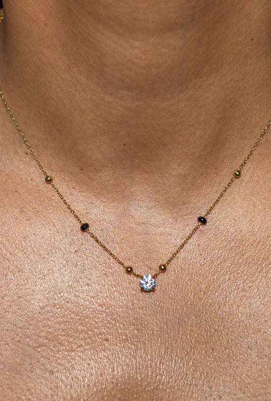 Close-up of a person wearing the gold Avira Mangalsutra Necklace by Kirosa London, featuring a delicate chain with a single round solitaire crystal pendant flanked by tiny gold and black beads