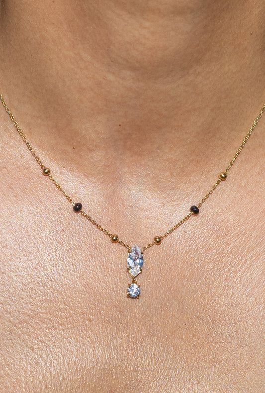 Close-up of a model wearing a Kirosa London gold mangalsutra necklace featuring a vertical drop pendant with a marquise-cut crystal and dangling round stone, flanked by signature black and gold beads.