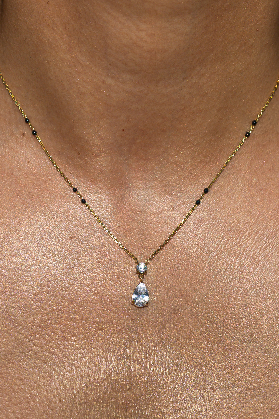 Close-up of a model wearing the Kirosa London gold Saha Mangalsutra Necklace featuring a vertical drop pendant with a small round crystal above a pear-cut teardrop stone, flanked by signature black beads.