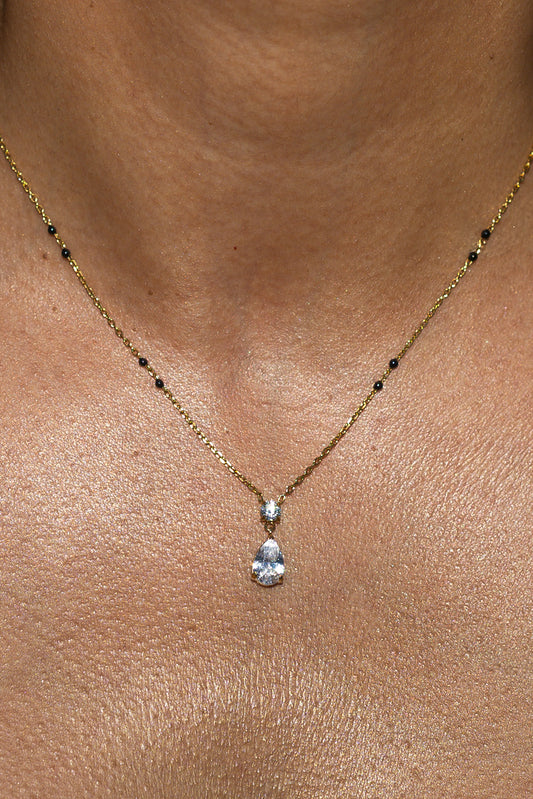 Close-up of a model wearing the Kirosa London gold Saha Mangalsutra Necklace featuring a vertical drop pendant with a small round crystal above a pear-cut teardrop stone, flanked by signature black beads.