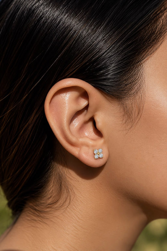 A close-up of a person's ear wearing a small four-stone diamond stud earring with a silver-toned setting.