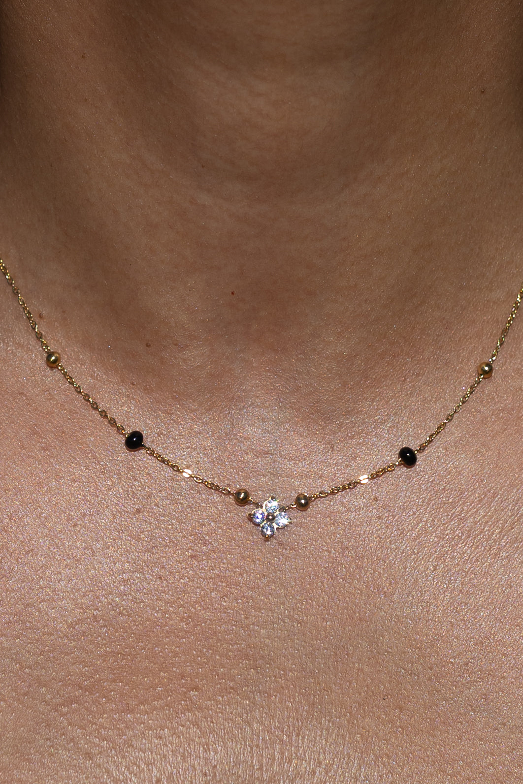 Close-up of a model wearing the Kirosa London gold Samya Mangalsutra Necklace, featuring a four-stone floral crystal pendant flanked by signature black and gold beads.