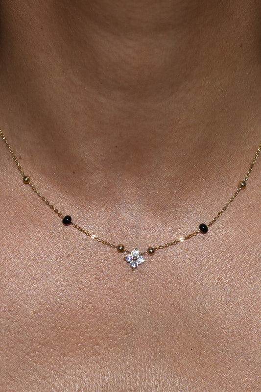 Close-up of a model wearing the Kirosa London gold Samya Mangalsutra Necklace, featuring a four-stone floral crystal pendant flanked by signature black and gold beads.